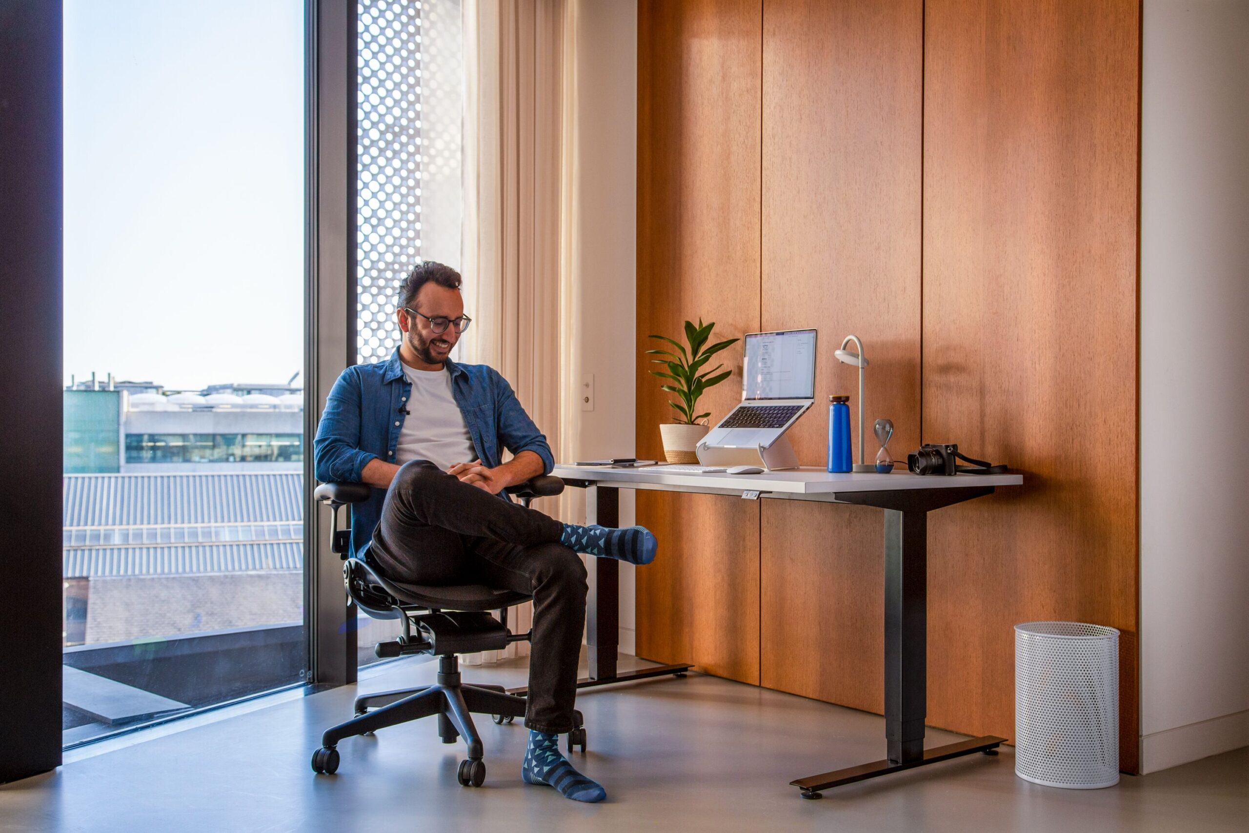 Homem sorri sentado em sua cadeira ergonômica Herman Miller