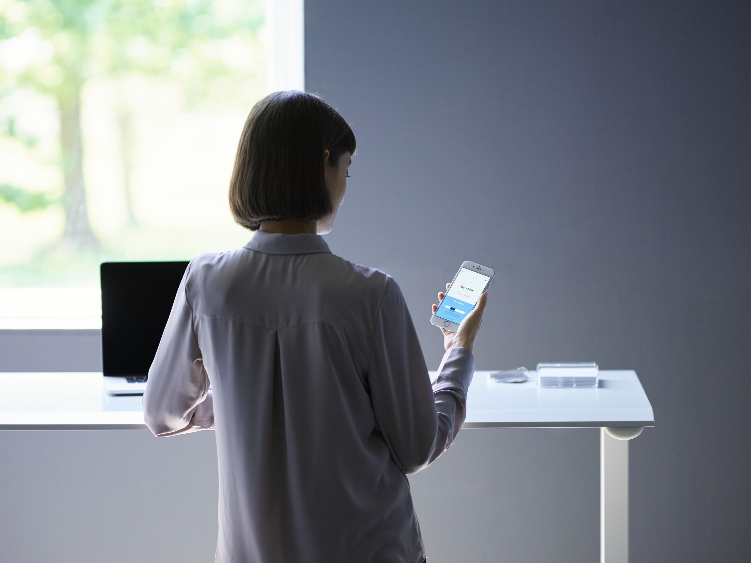Mulher confere o seu celular enquanto trabalha em pé em sua standing desk