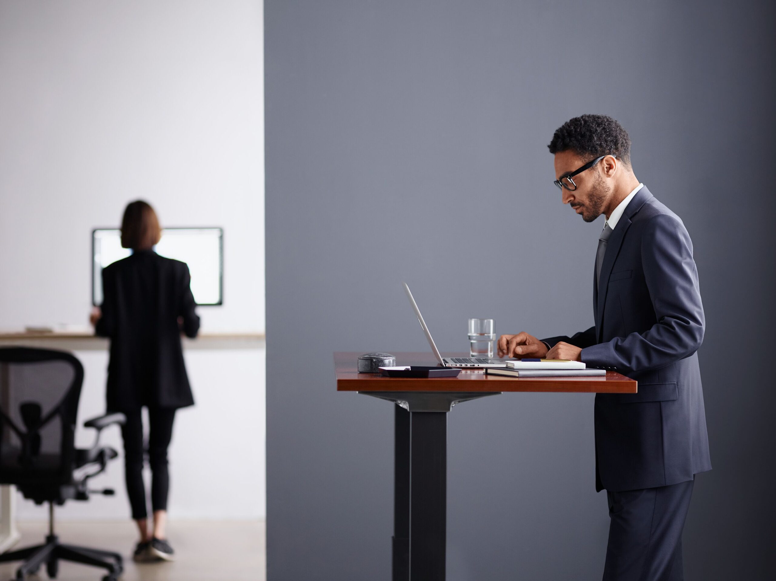 Homem com roupa de escritório utiliza seu notebook em pé em uma mesa alta