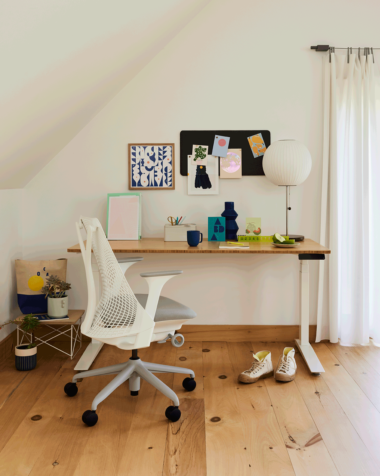 Home office moderno com cadeira ergonômica branca, mesa ajustável em altura e decoração minimalista em ambiente iluminado naturalmente.