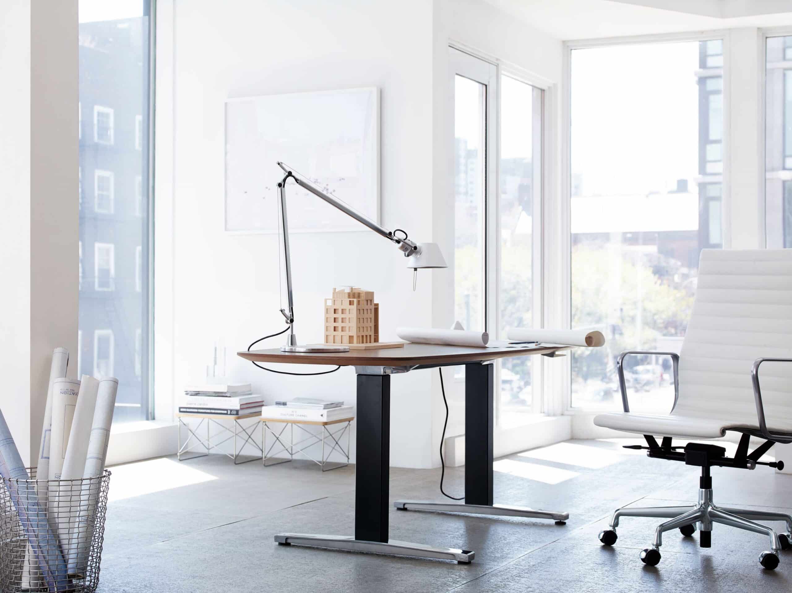 Escritório moderno com mesa de trabalho, cadeira ergonômica, luminária articulada e ampla iluminação natural proporcionada por janelas panorâmicas.
