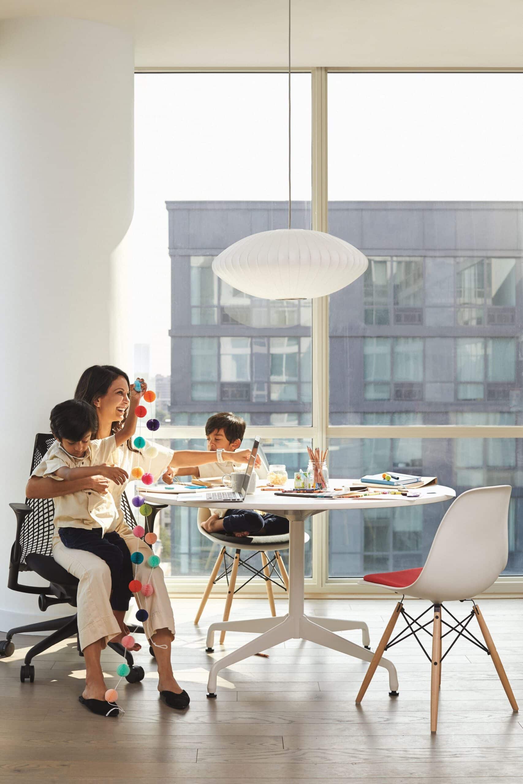 Família reunida em mesa de trabalho e estudos em ambiente residencial moderno com móveis de design e ampla iluminação natural.