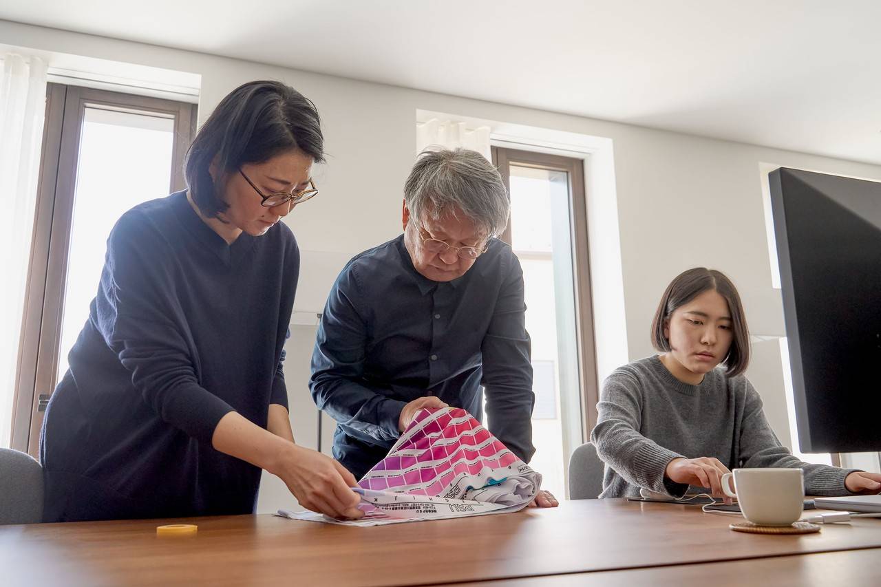 Naoto Fukasawa e outras duas mulheres concentrados em uma mesa de escritório