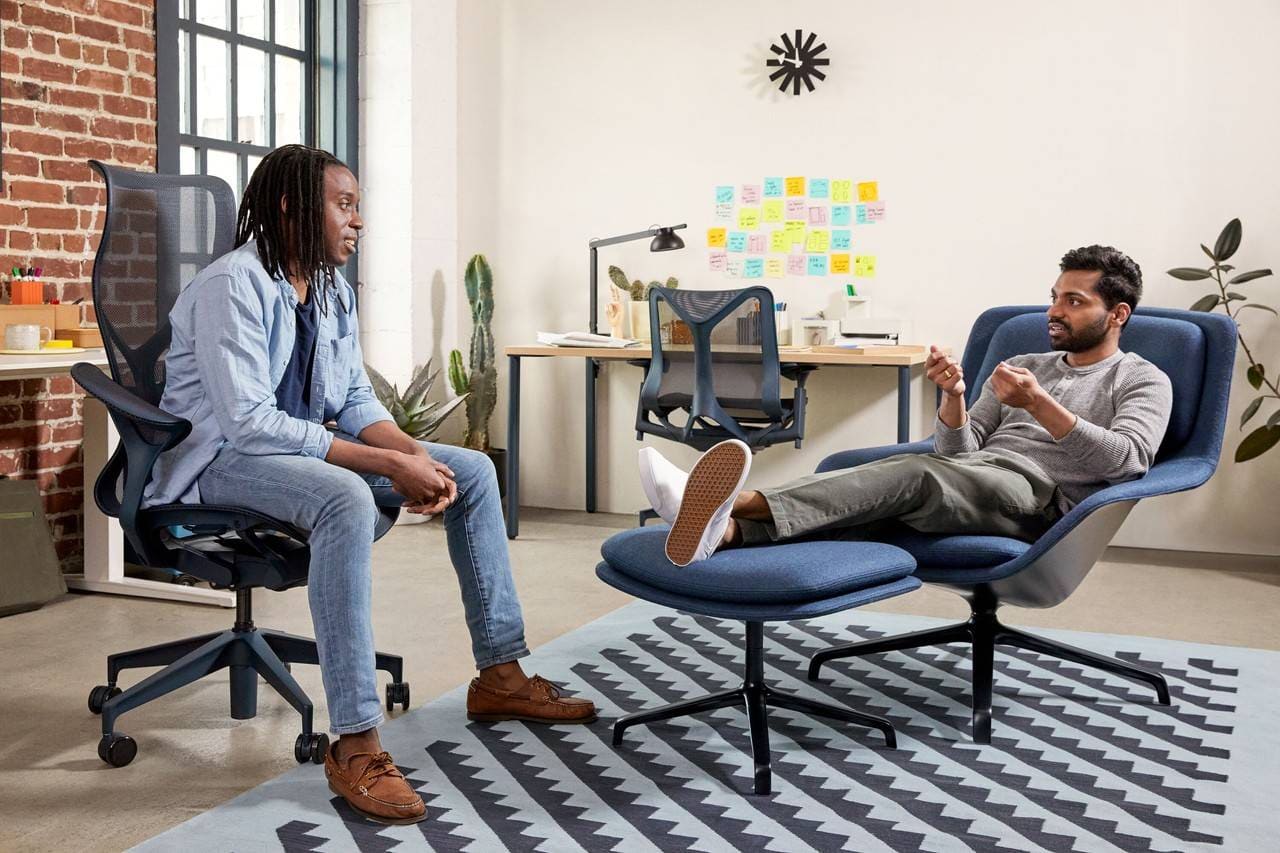 dois homens conversando sentados em uma poltrona eames e em uma cadeira ergonômica