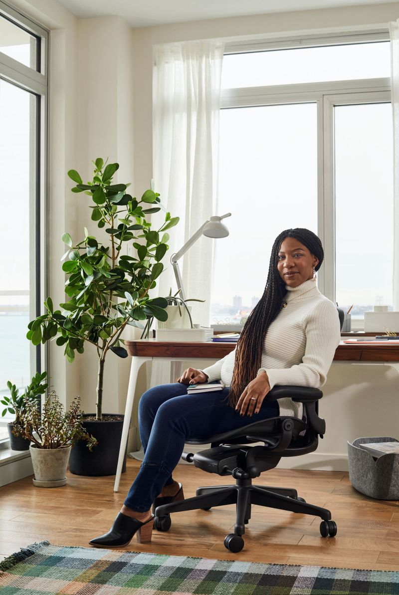 mulher negra sentada em uma cadeira aeron em seu home office