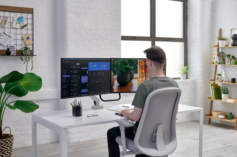 Homem trabalhando em mesa com dois monitores e planta