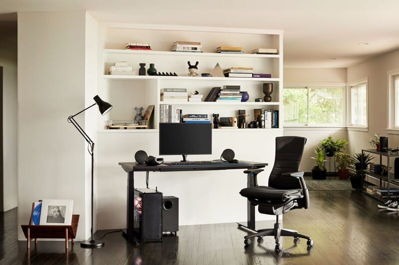 Escritório moderno com mesa, cadeira ergonômica e estante.