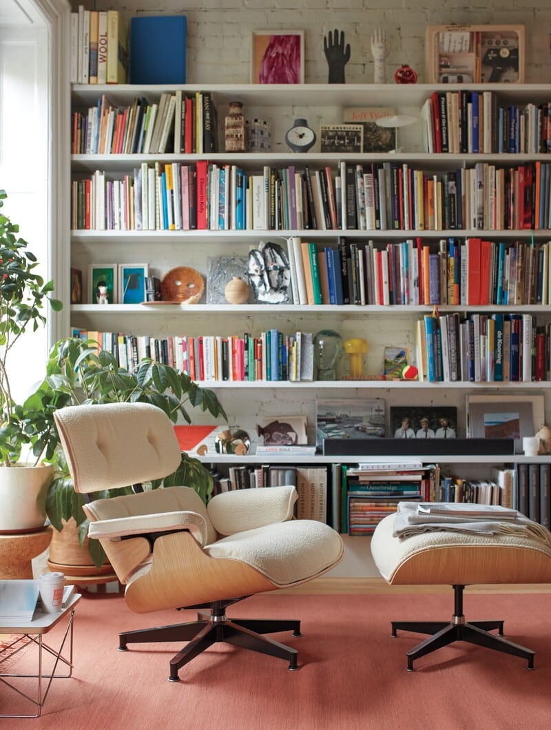 Sala com poltrona moderna e estante cheia de livros.